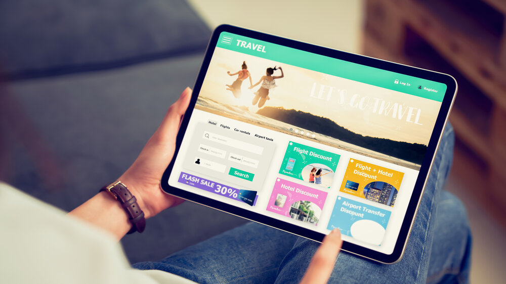 In Händen haltendes digitales Tablet mit Anwendung zur Buchung von Flug, Reise, Suche, Ticket Urlaub und Hotel auf Onlineplattformen. 