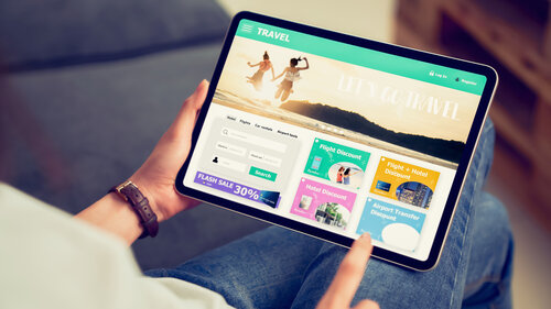 In Händen haltendes digitales Tablet mit Anwendung zur Buchung von Flug, Reise, Suche, Ticket Urlaub und Hotel auf Onlineplattformen. 